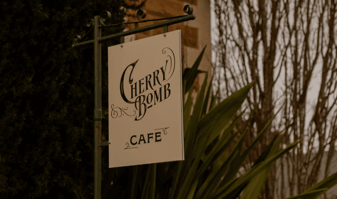The Cherry Bomb Cafe hanging sign on the heritage cottage exterior, surrounded by greenery
